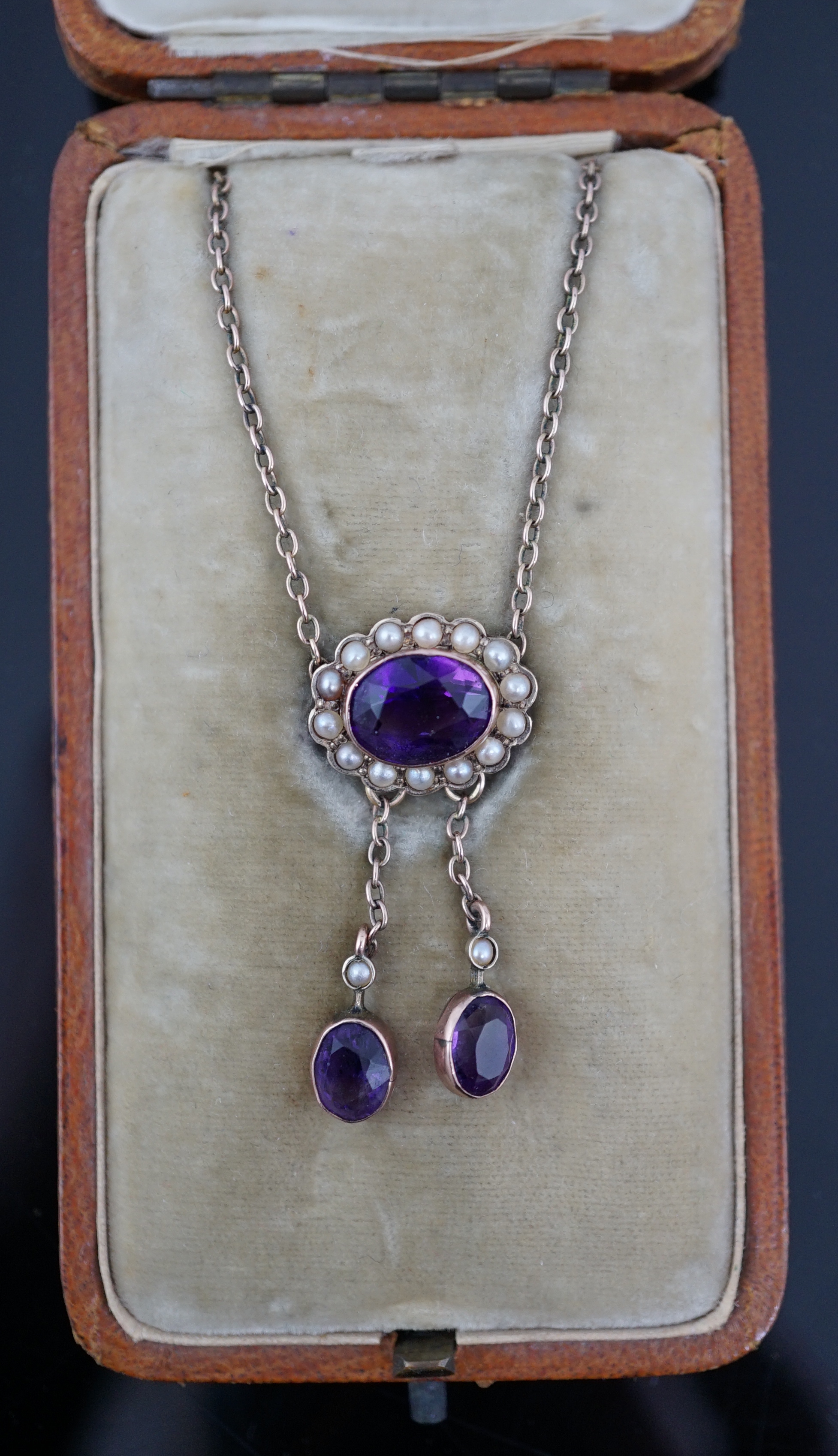 A cased Edwardian 9ct gold, amethyst and seed pearl cluster set double drop pendant necklace